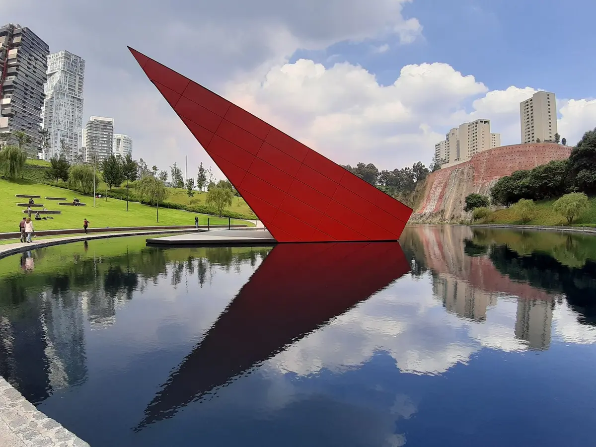 Escultura roja reflejada en el lago del Parque La Mexicana, rodeado de torres residenciales, uno de los atractivos de vivir en Santa Fe CDMX